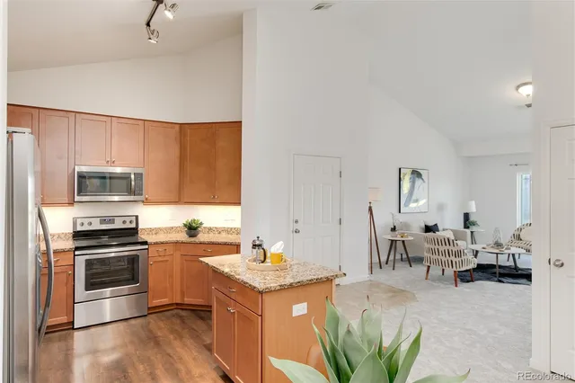 a kitchen with stainless steel appliances kitchen island granite countertop a stove top oven a sink a dining table and chairs with wooden floor