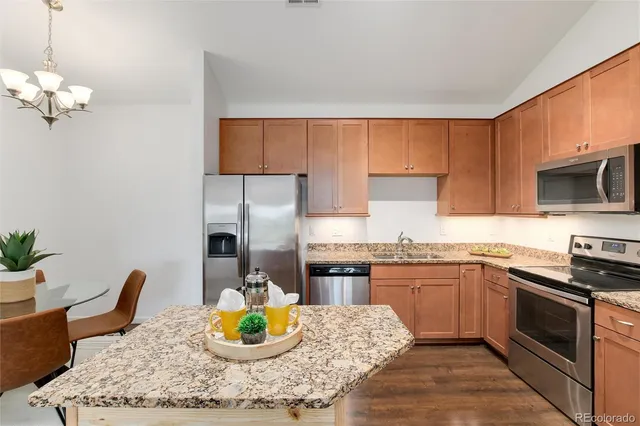 a kitchen with stainless steel appliances granite countertop a stove top oven a sink a dining table and chairs with wooden floor