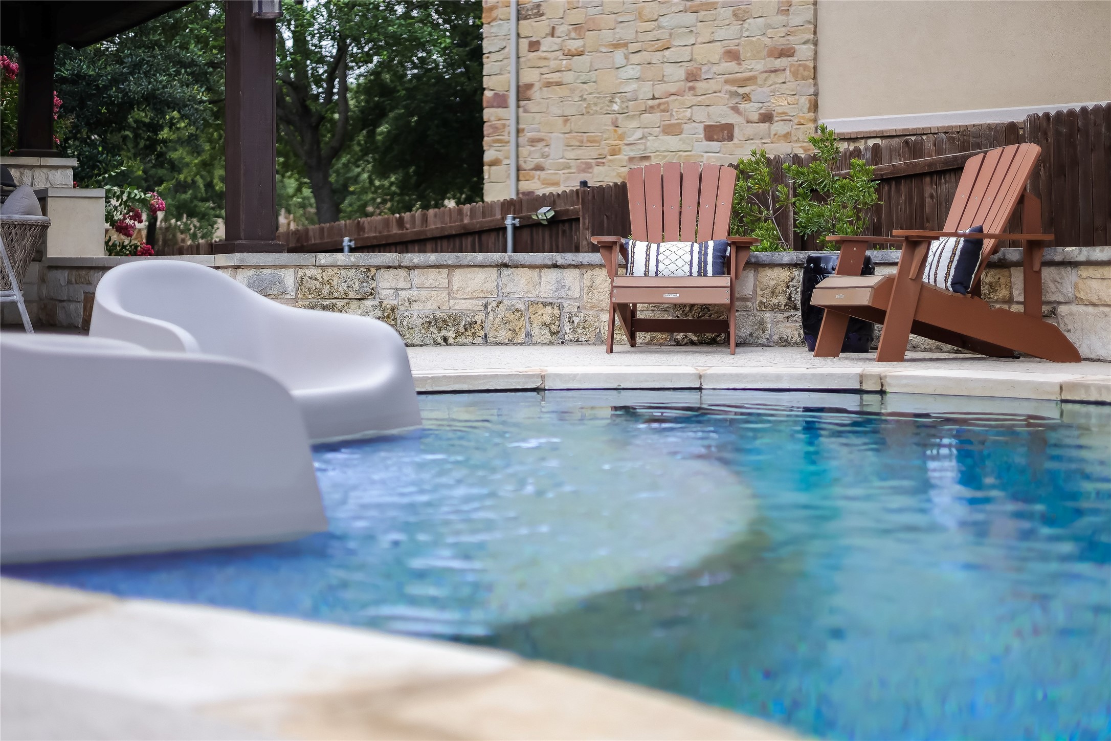 401 Bluff View Road Cedar Park, TX 78613 - Photo 7 of 40 A tranquil outdoor haven features a refreshing pool, inviting Adirondack chairs, and a natural stone retaining wall.