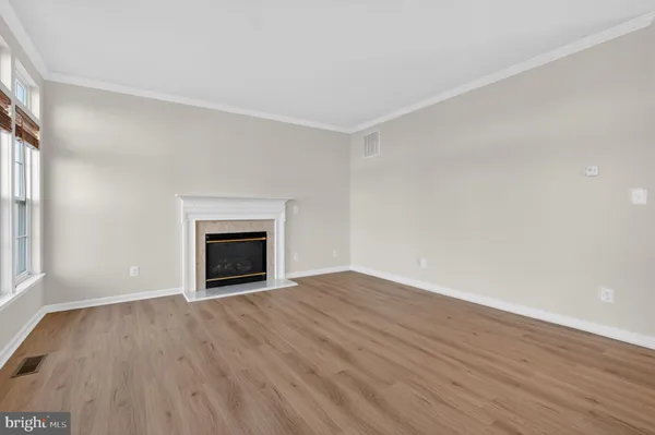 a view of an empty room with wooden floor fireplace and a window