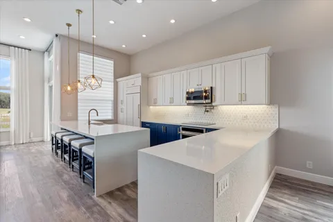 a kitchen with stainless steel appliances granite countertop a stove top oven a refrigerator a sink and white cabinets with wooden floor