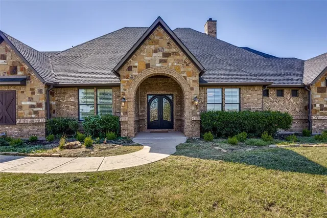 a view of a brick house with potted plants and a large tree