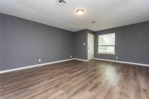 a view of an empty room with wooden floor and window