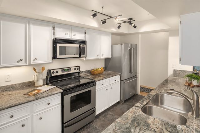 a kitchen with granite countertop a sink stainless steel appliances and white cabinets
