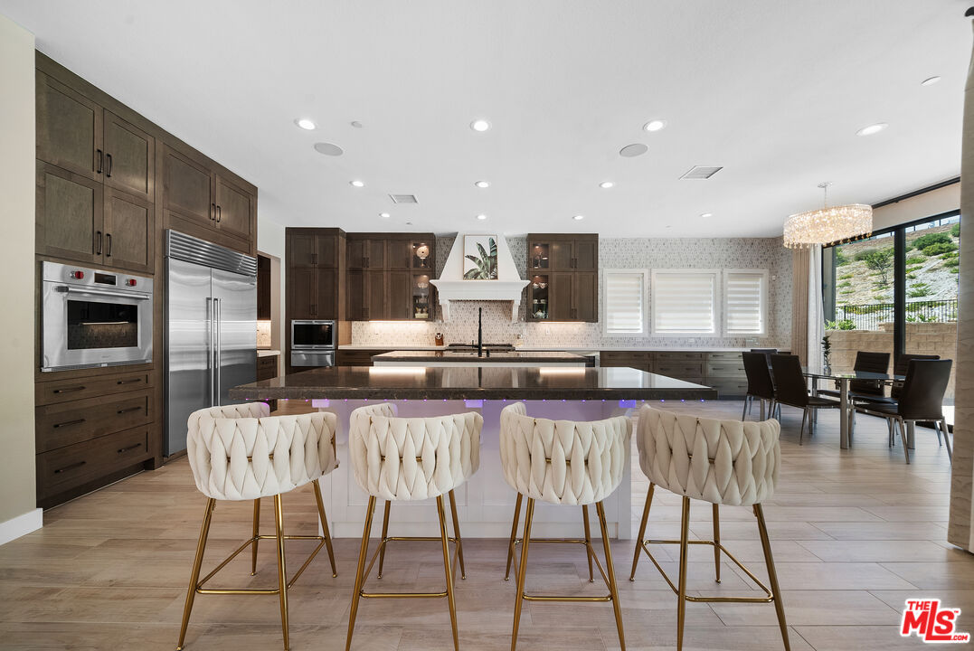 20517 Deer Grass Court Porter Ranch, CA 91326 - Photo 21 of 75 a kitchen with stainless steel appliances kitchen island granite countertop a refrigerator a stove a dining table and chairs with wooden floor