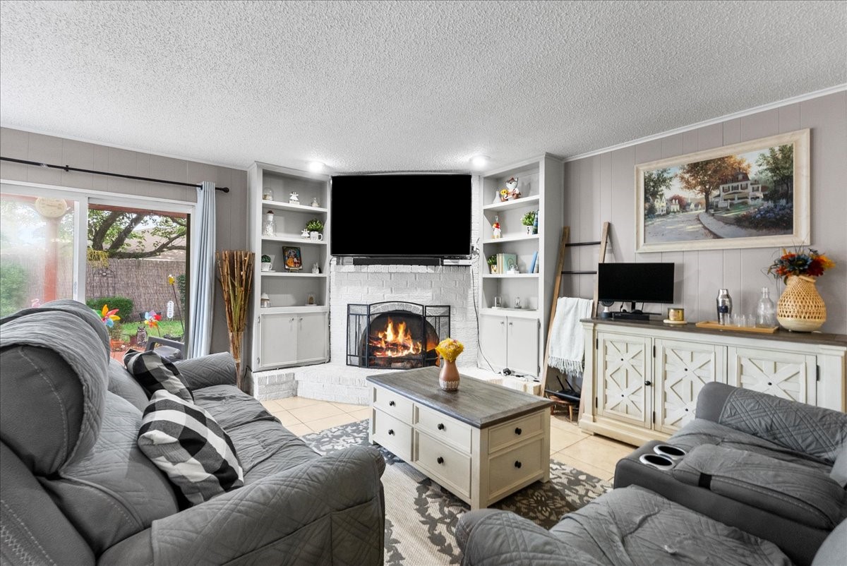 883 Silverpines Road Houston, TX 77062 - Photo 6 of 38 Cozy living room with a fireplace, built-in shelves, and a mounted TV. Features room for comfortable seating, a large sliding glass doors with garden views, and a bright, inviting atmosphere. Perfect for relaxing and entertaining.