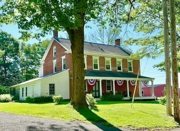 a view of a brick house with a big yard plants and large trees