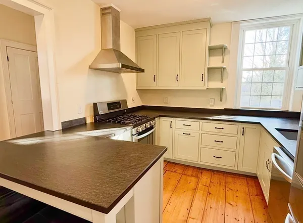 a kitchen with granite countertop a stove a sink and white cabinets with wooden floor