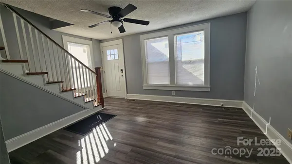 a view of an empty room with wooden floor and fan