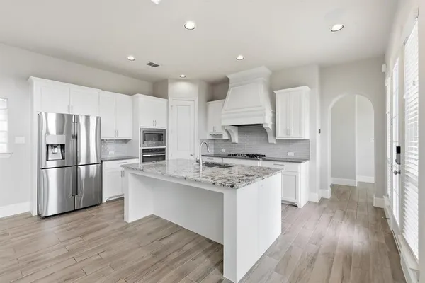 a kitchen with stainless steel appliances granite countertop a refrigerator a stove a sink and white cabinets with wooden floor