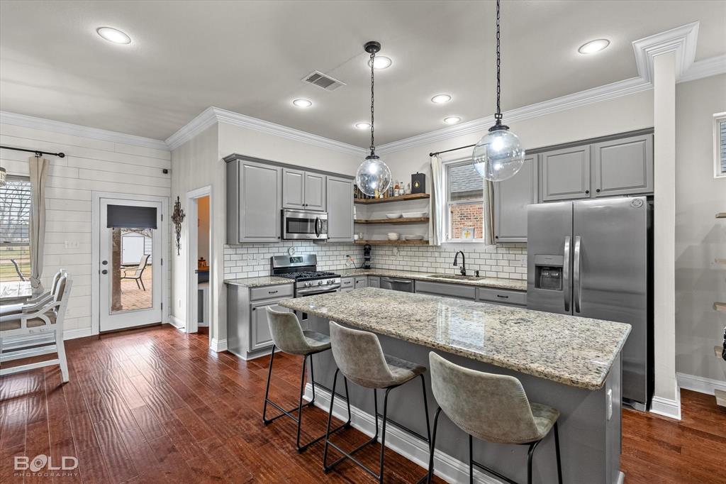946 Maize Street Bossier City, LA 71111 - Photo 19 of 39 a kitchen with stainless steel appliances granite countertop a stove a refrigerator a kitchen island a sink and white cabinets with wooden floors