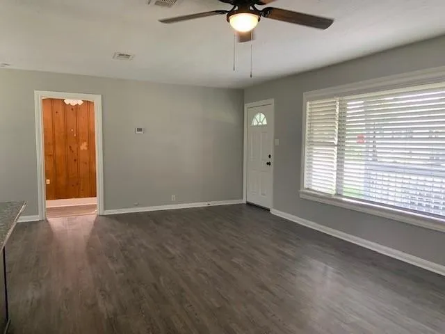 an empty room with wooden floor fan and windows