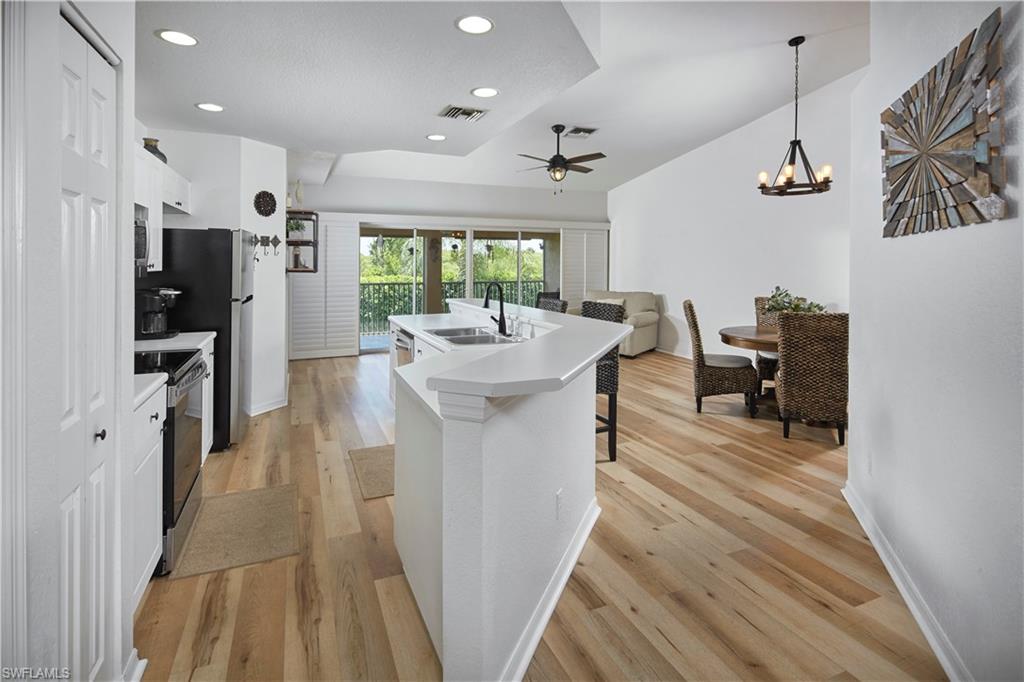 a kitchen with stainless steel appliances kitchen island granite countertop a refrigerator a sink dishwasher a stove and a dining table with wooden floor