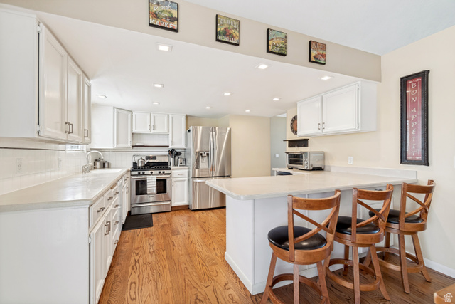 9832 Falconhurst Drive Sandy, UT 84092 - Photo 8 of 29 Bright kitchen featuring white cabinetry, stainless steel appliances, a white tile backsplash, light-toned countertops, and wood-finish flooring