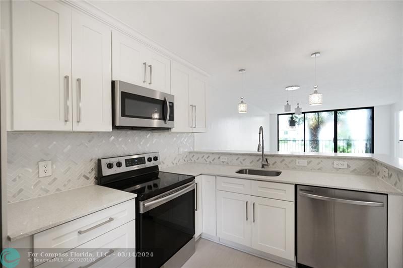 a kitchen with stainless steel appliances granite countertop a sink a stove a microwave and white cabinets