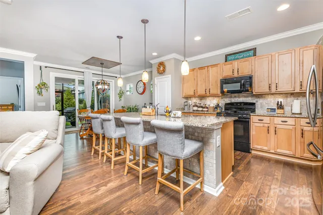 a kitchen with stainless steel appliances kitchen island granite countertop a stove a sink a dining table and chairs with wooden floor