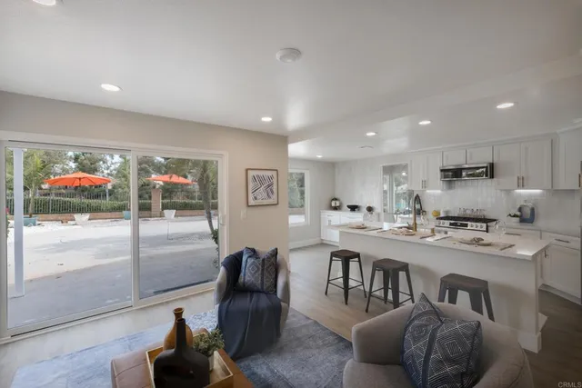 a living room with stainless steel appliances furniture a rug and a kitchen view