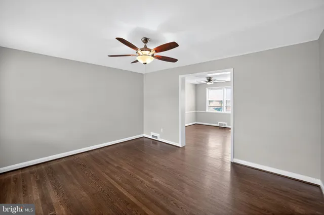 a view of an empty room with wooden floor and a ceiling fan