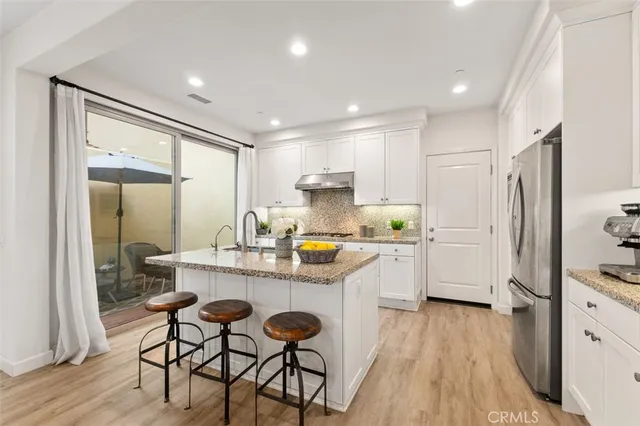 a kitchen with stainless steel appliances granite countertop a refrigerator a sink dishwasher a stove and white cabinets with wooden floor