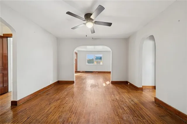 an empty room with wooden floor chandelier fan and windows