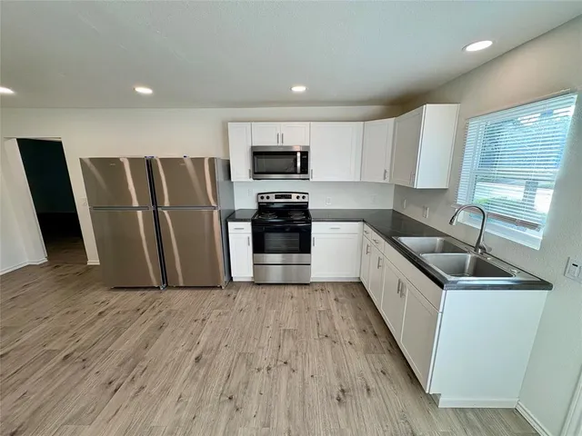 a kitchen with granite countertop a refrigerator a sink a stove a microwave and wooden floor