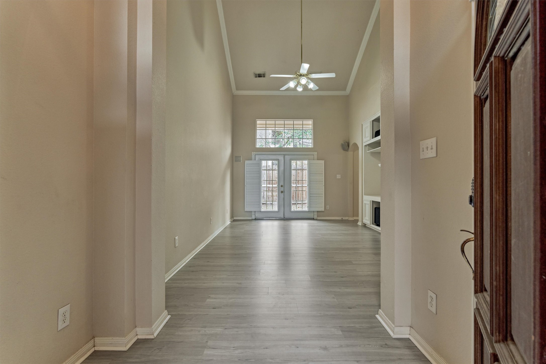 14420 Walters Road, Unit 26 Houston, TX 77014 - Photo 8 of 45 You walk into a bright, open living area with high ceilings and light gray flooring. French doors open to a rear patio, and built-in shelving adds functionality. The space is well-lit with a ceiling fan and ample natural light.