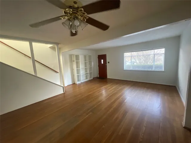 an empty room with wooden floor chandelier fan and windows