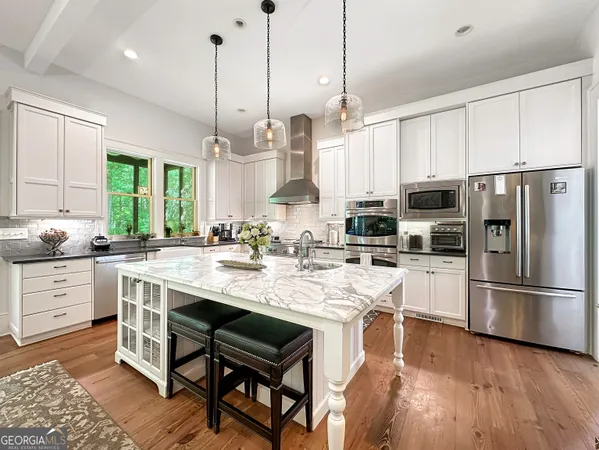 a kitchen with stainless steel appliances granite countertop a refrigerator a sink dishwasher a stove and white cabinets with wooden floor