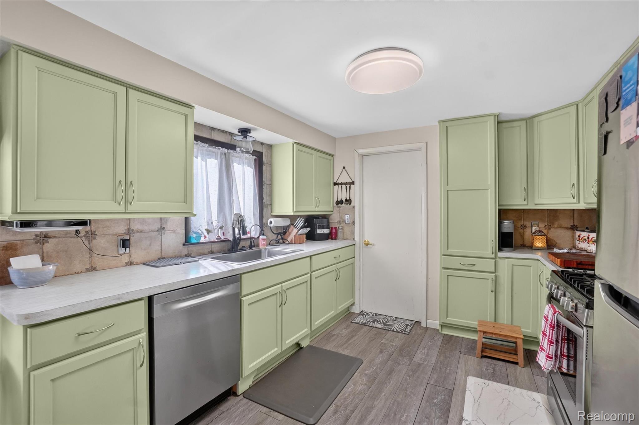 7178 Riegler Street Grand Blanc, MI 48439 - Photo 8 of 31 Kitchen featuring sage green cabinetry, a double basin sink, stainless steel dishwasher, wood-finish flooring, and a flush mount ceiling light