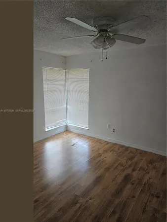 an empty room with wooden floor a ceiling fan and windows
