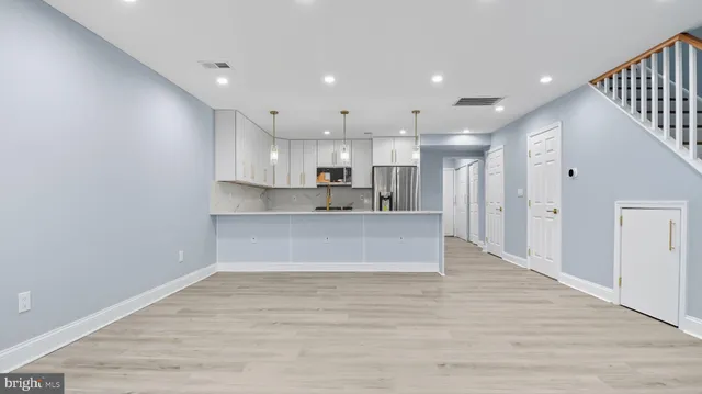 a large kitchen with kitchen island a sink dishwasher a refrigerator and white cabinets with wooden floor