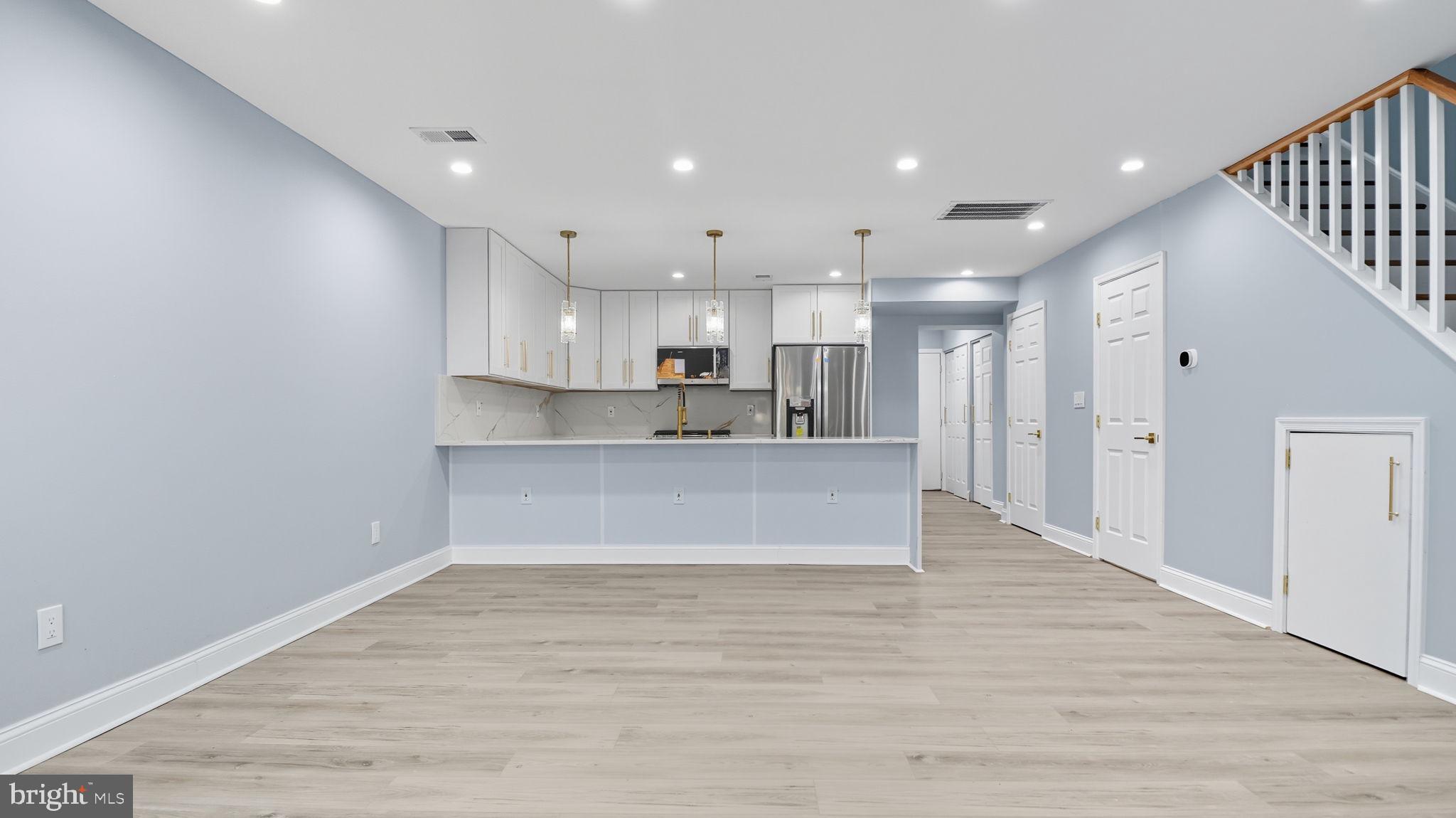 2238 15th Street Northeast Washington, DC 20018 - Photo 7 of 38 a large kitchen with kitchen island a sink dishwasher a refrigerator and white cabinets with wooden floor