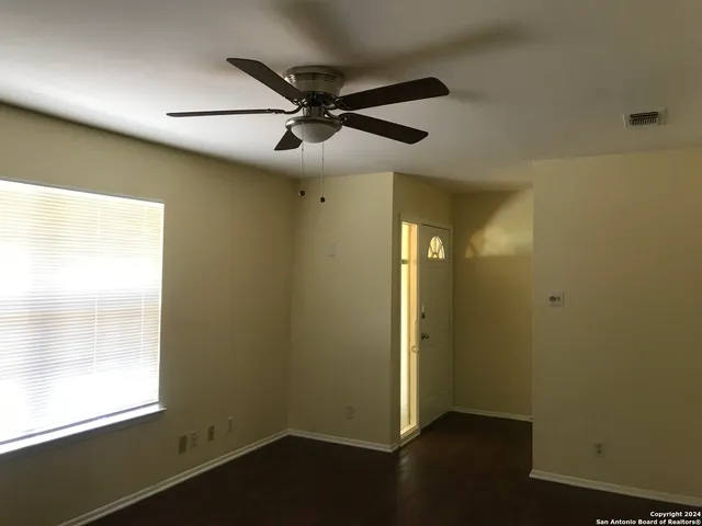 an empty room with wooden floor fan and windows