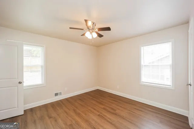 an empty room with wooden floor ceiling fan and windows