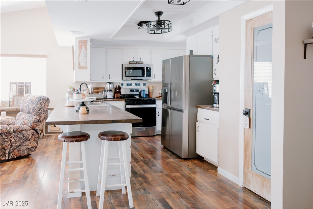1515 Darlene Way Boulder City, NV 89005 - Photo 6 of 22 Kitchen with white cabinetry, appliances with stainless steel finishes, a kitchen breakfast bar, a peninsula, and dark wood-type flooring