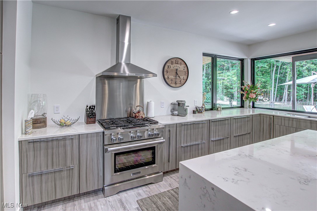 4385 Good Road Seville, OH 44273 - Photo 16 of 50 Kitchen featuring wall chimney exhaust hood, light stone countertops, light hardwood / wood-style flooring, high end stainless steel range, and gray cabinetry