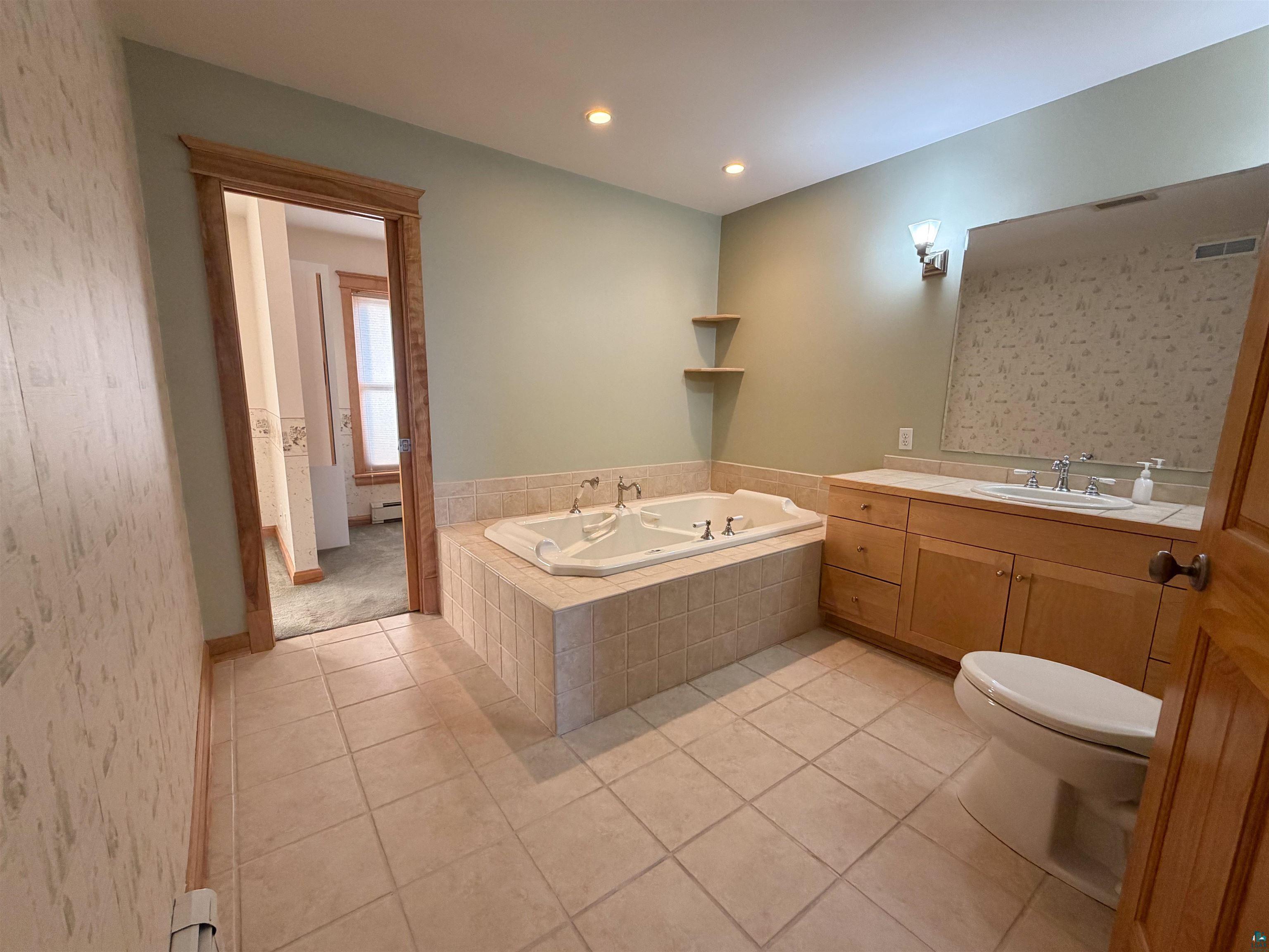 13 West 8th Street Duluth, MN 55806 - Photo 21 of 57 Spacious bathroom featuring a built-in jetted tub with tile surround, a wood-finish vanity with an integrated sink and mirror, tile flooring, and recessed lighting