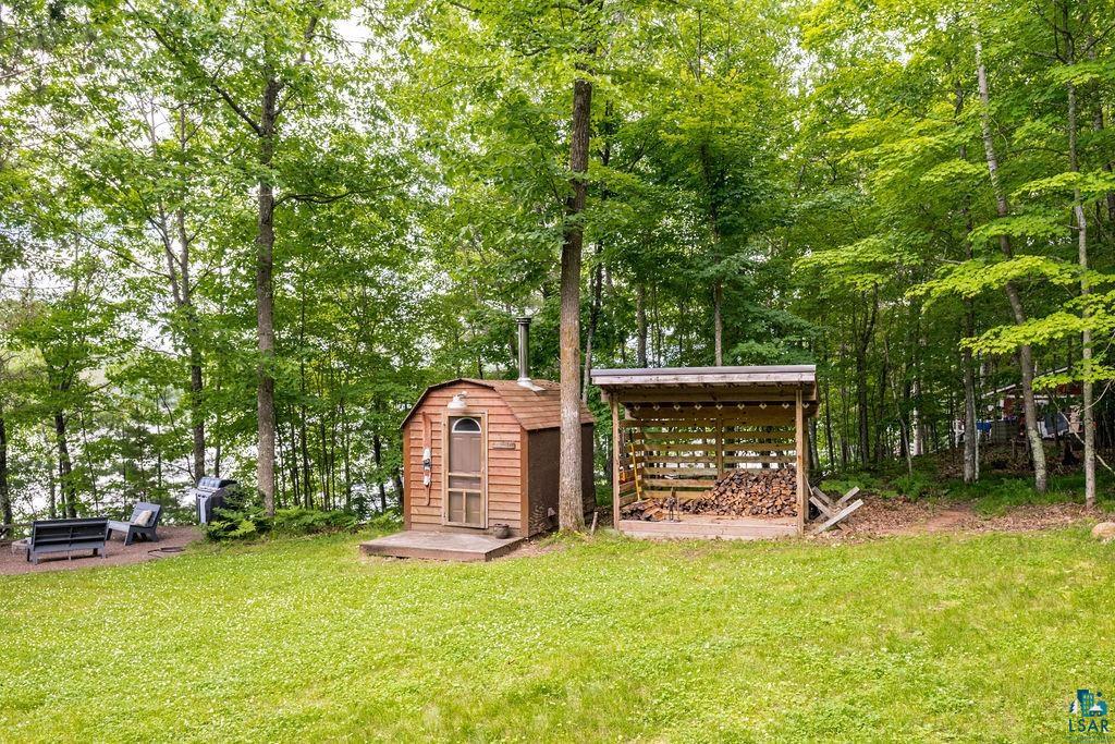 7338 South Maranatha Road Lake Nebagamon, WI 54849 - Photo 2 of 41 Lush green lawn with a wood-sided outbuilding featuring a small deck and a metal chimney