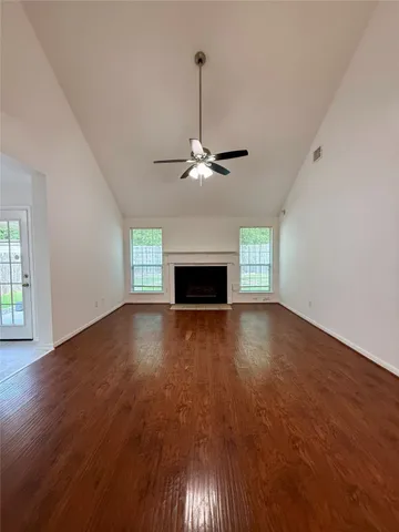 an empty room with wooden floor chandelier fan and windows