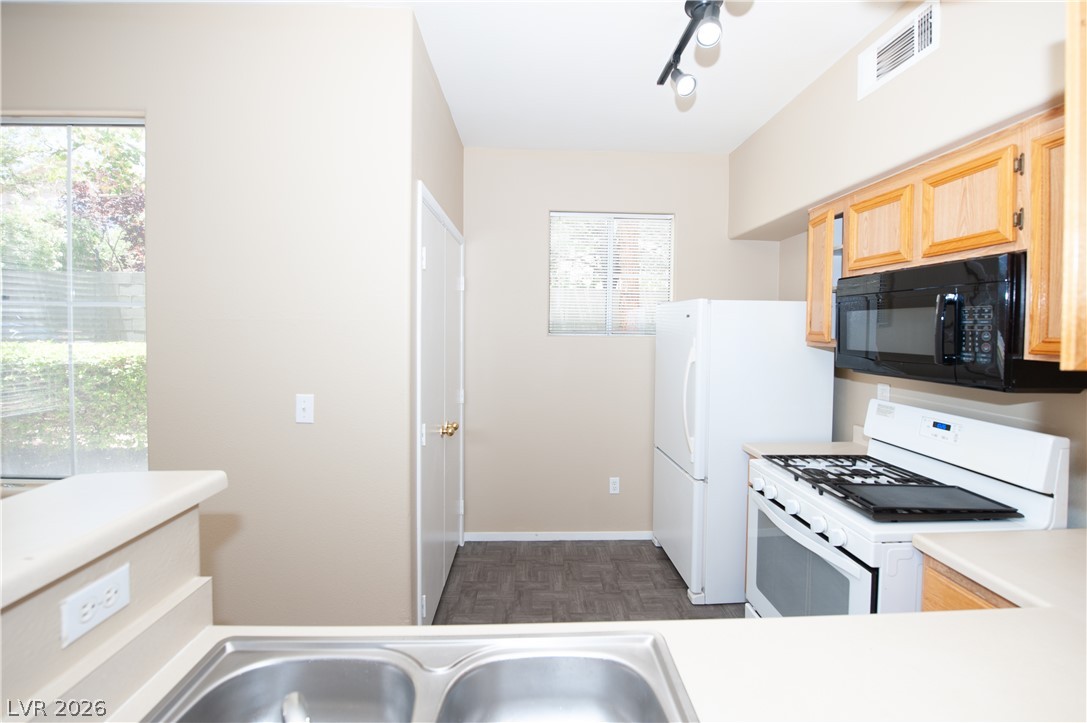 9050 West Warm Springs Road, Unit 1132 Las Vegas, NV 89148 - Photo 9 of 21 A compact culinary space features classic wood cabinets and modern white appliances for efficient meal preparation.