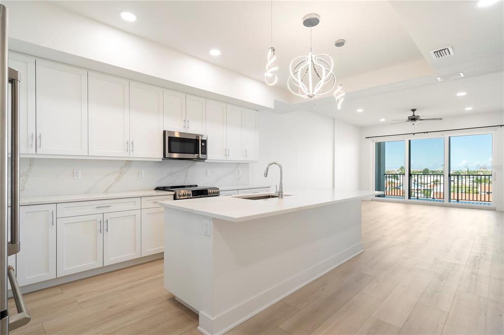 400 150th Avenue, Unit 501 Madeira Beach, FL 33708 - Photo 42 of 76 a kitchen with stainless steel appliances granite countertop a stove top oven a sink dishwasher a dining table and chairs with wooden floor