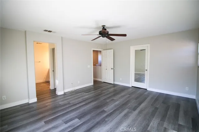 a view of an empty room with wooden floor and a ceiling fan