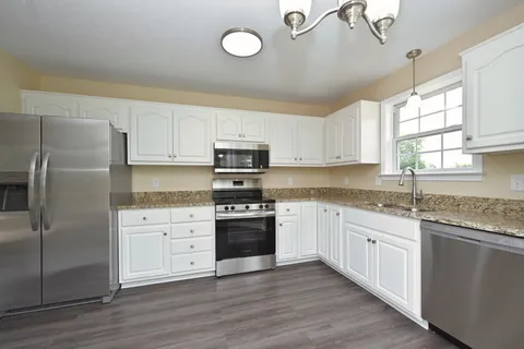 a kitchen with stainless steel appliances granite countertop a stove a sink dishwasher a refrigerator and white cabinets with wooden floor