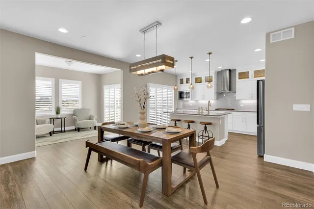 a kitchen with stainless steel appliances kitchen island granite countertop a stove a refrigerator a sink a dining table and chairs with wooden floor