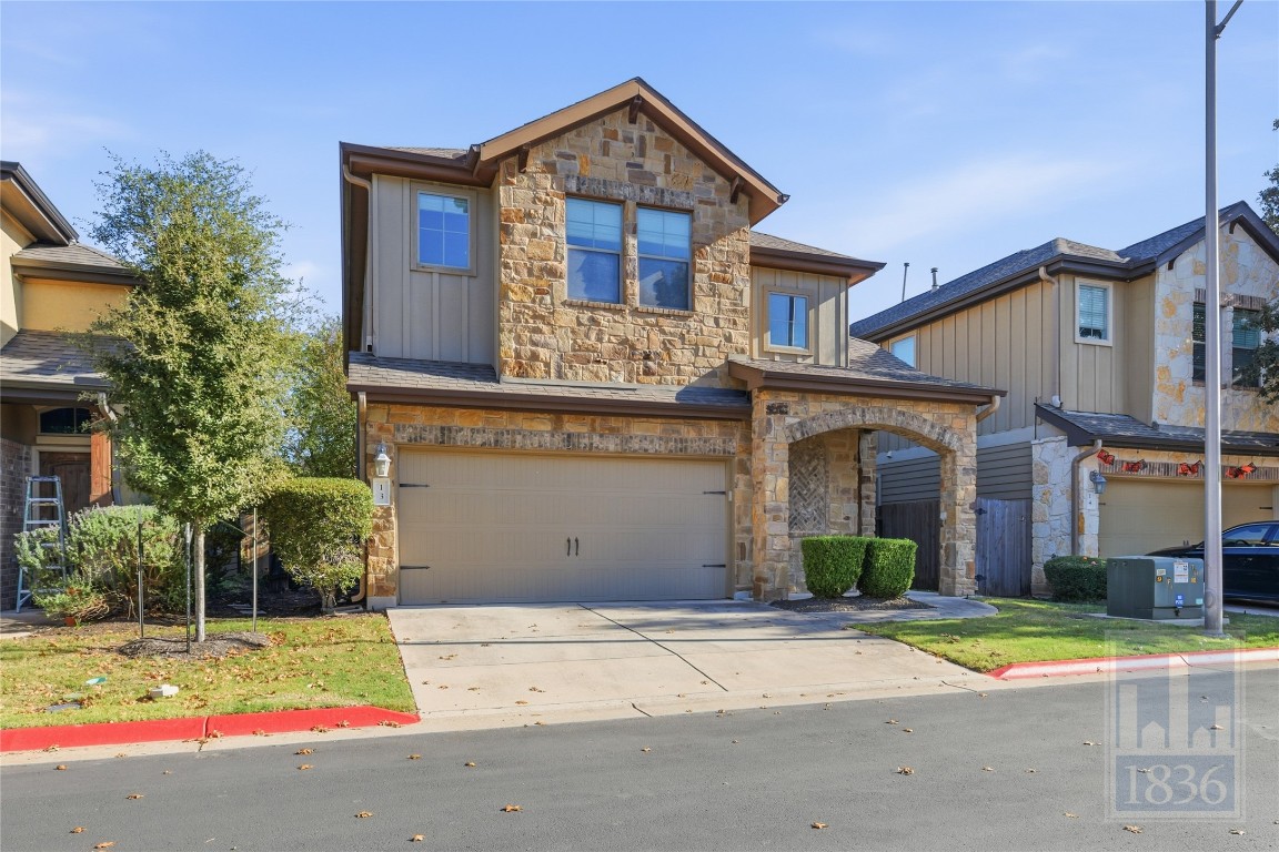 View of front of property featuring stone siding, driveway, an attached garage, and board and batten siding