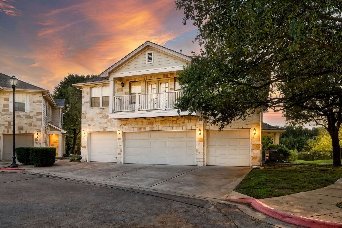 View of front of house featuring a balcony, stone siding, driveway, and an attached garage