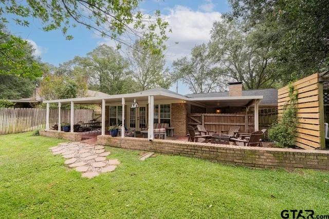 front view of a house with a yard table and chairs and large trees