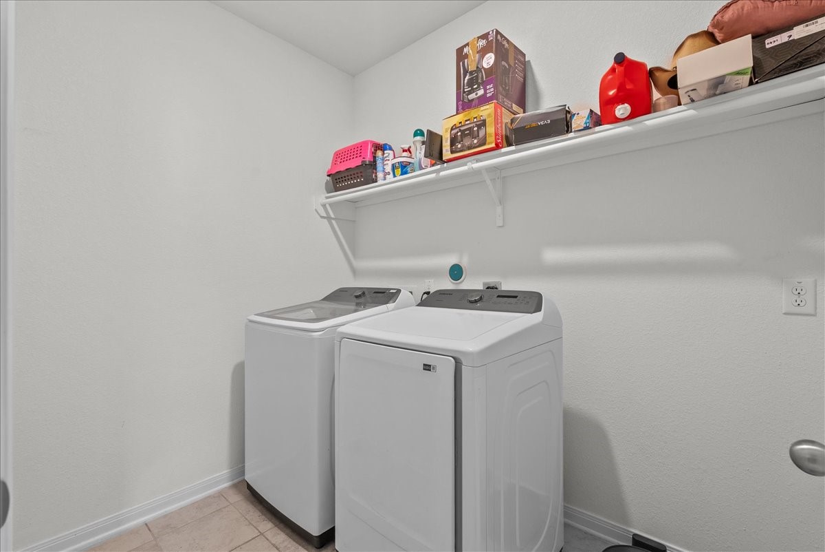 2320 Rosemary Street Rosenberg, TX 77469 - Photo 34 of 40 This photo shows a laundry room with a washer and dryer set against a white wall. There's a shelf above for storage, holding various household items and supplies. The space is compact and functional.