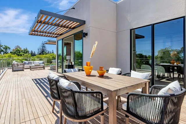 a view of a roof deck with table and chairs a barbeque with wooden floor and fence