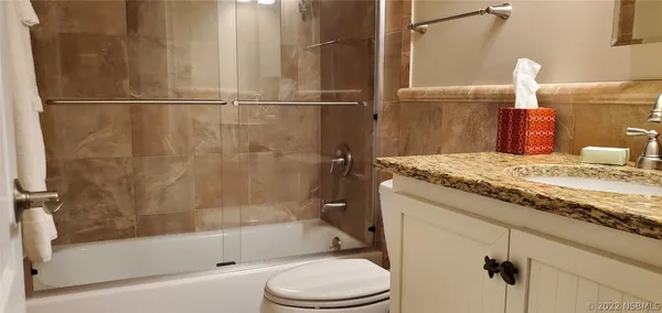 a bathroom with a granite countertop bathtub shower sink vanity and toilet
